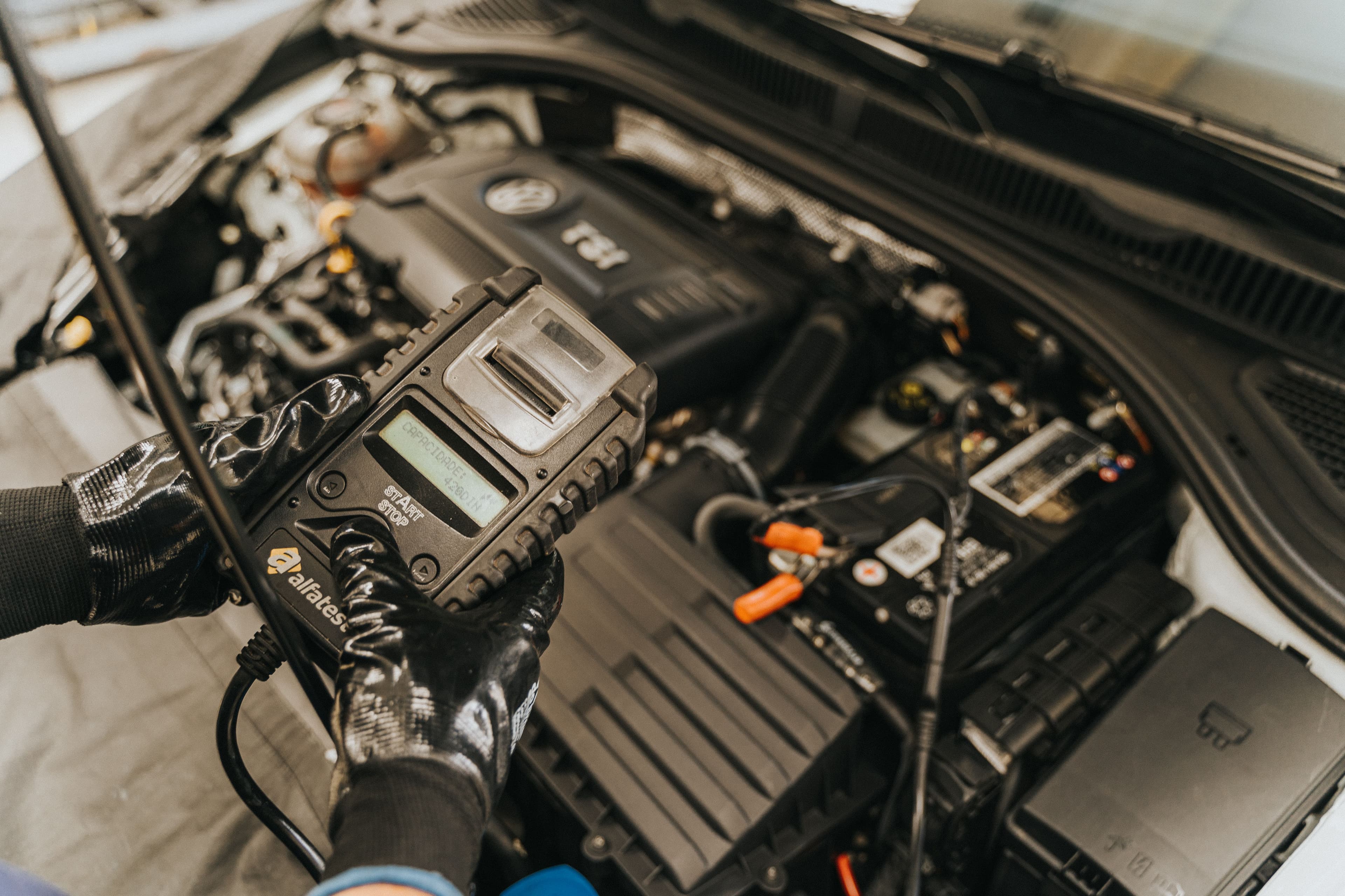 Technician using a diagnostic scan tool beside an open vehicle engine bay