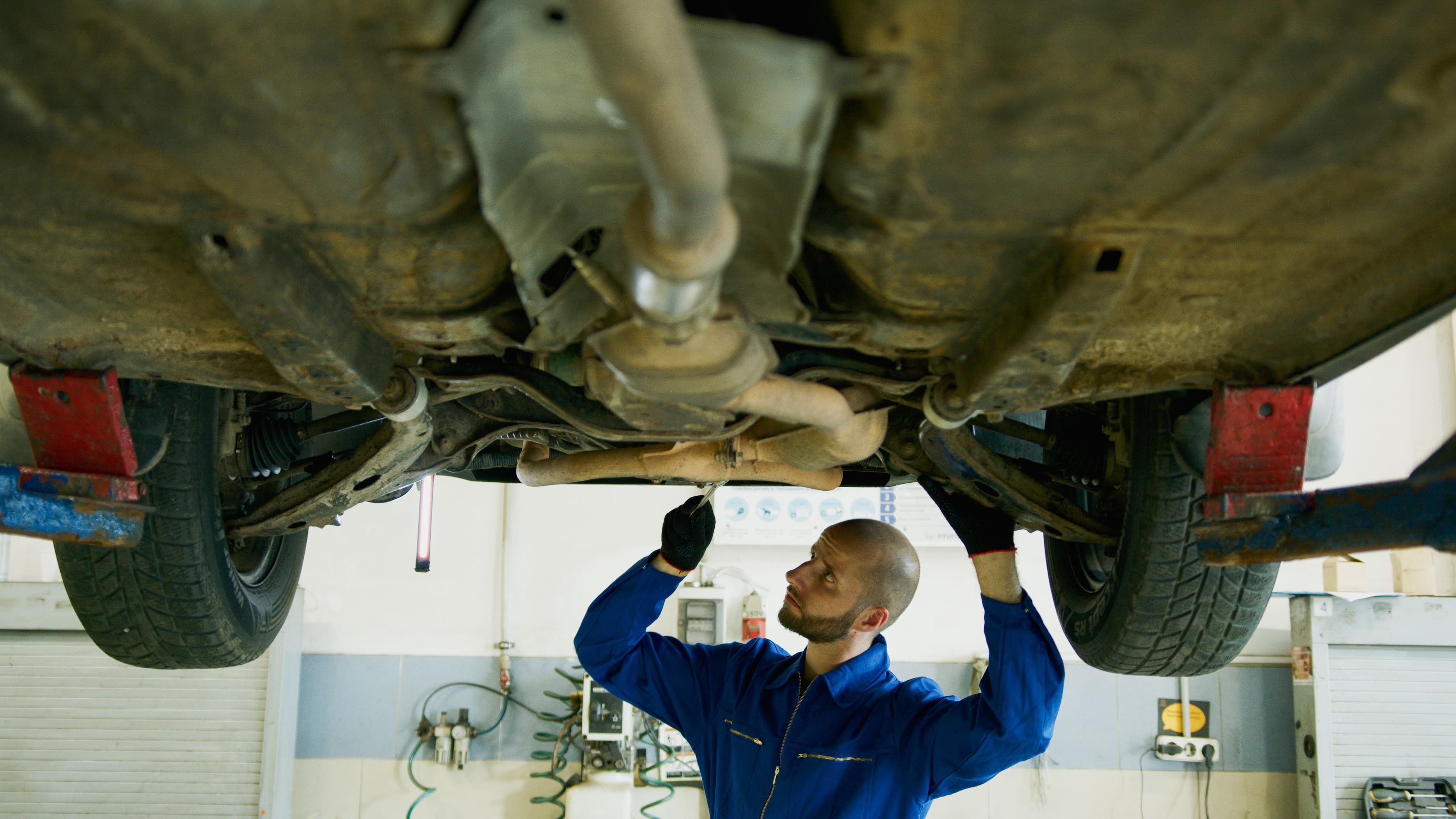 Mechanic inspecting the underside of a vehicle on a workshop lift before transmission service
