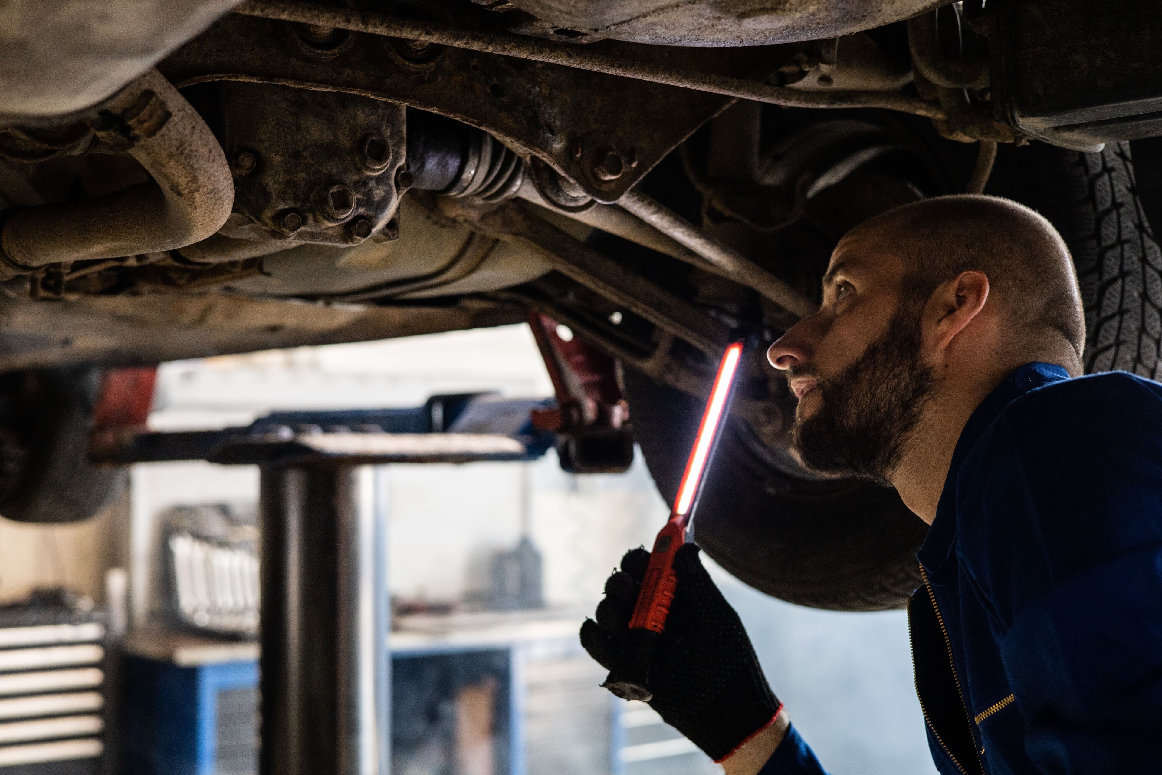 Mechanic using an inspection light beneath a raised vehicle to check front driveline components